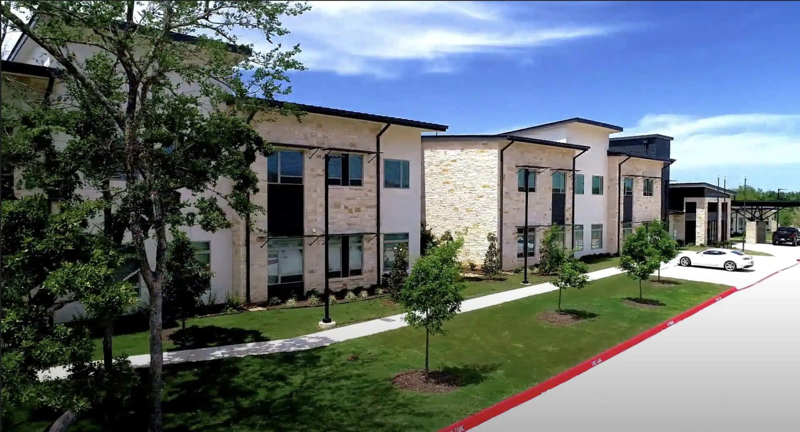 The stone and stucco exterior of VIVERE Life College Station, with young trees along the front walk